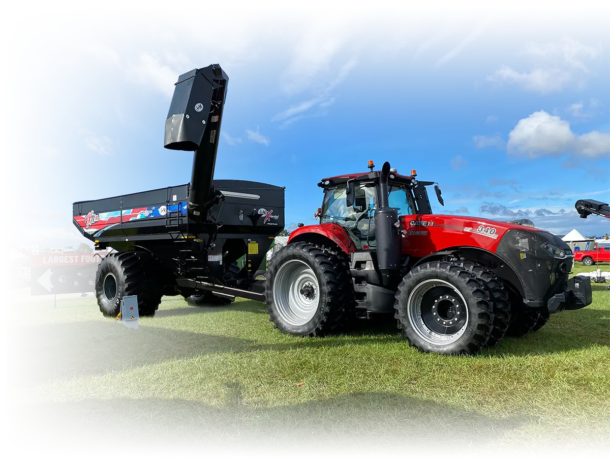 a green grain cart with the auger extended sitting in a field at a farm show.
